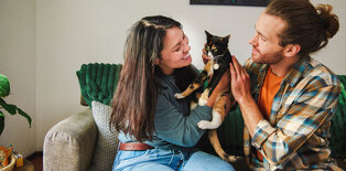 Young women and man sitting on couch with cat
