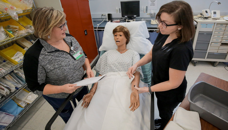 photo of Nursing Assistant student practicing on a dummy patient in a hospital bed.