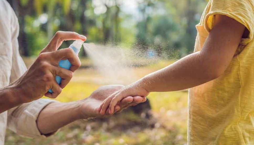 Mother spraying bug repellant on child