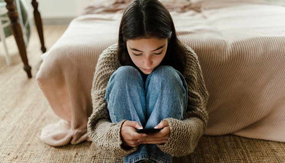 teenage girl sitting on floor looking at her phone