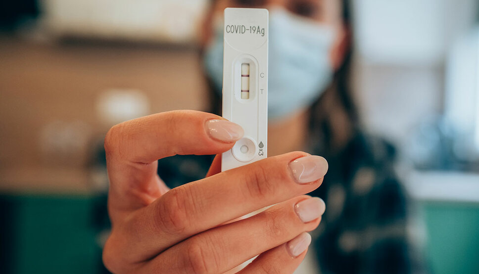 Photo of a woman holding up a COVID test