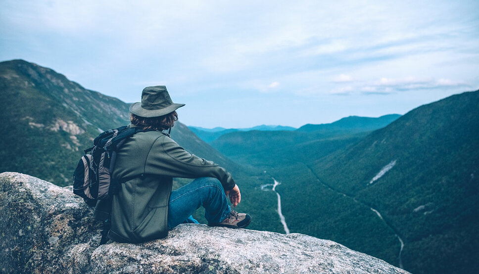 Photo of a man sitting on top of a mountain looking out at the view