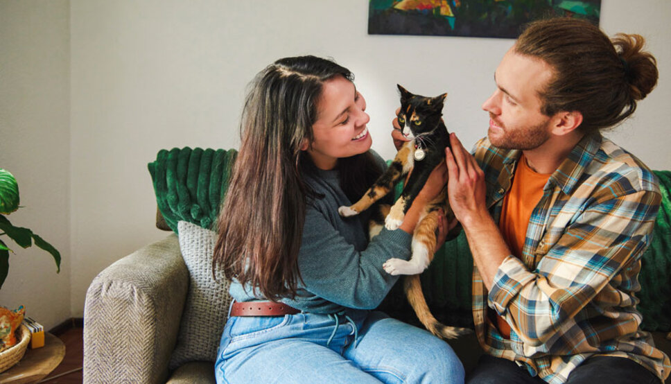 Young women and man sitting on couch with cat