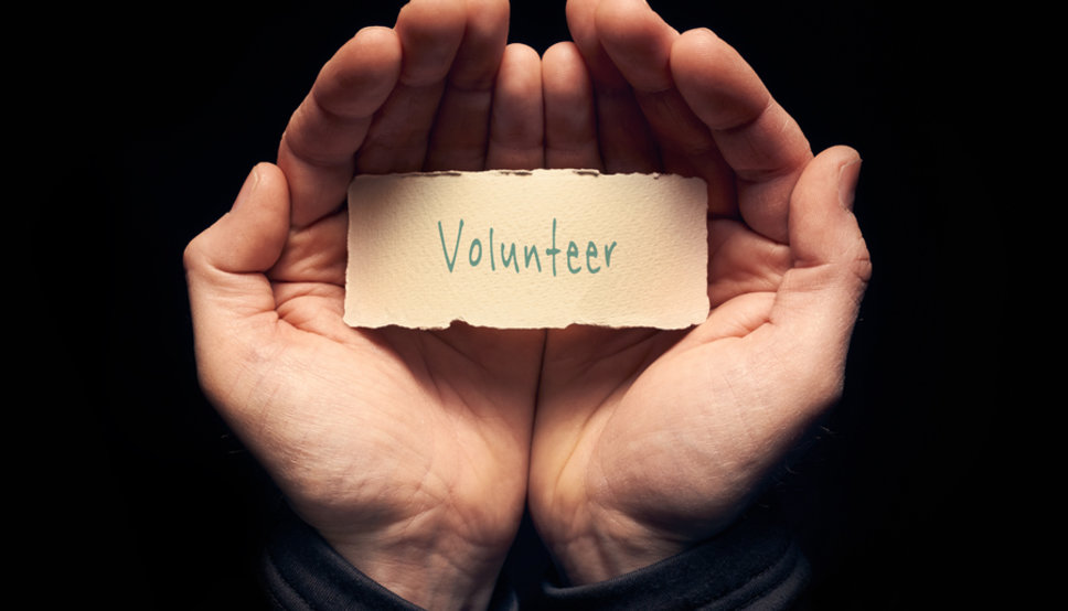 Two hands cupped together and holding a card that says "Volunteer" on it
