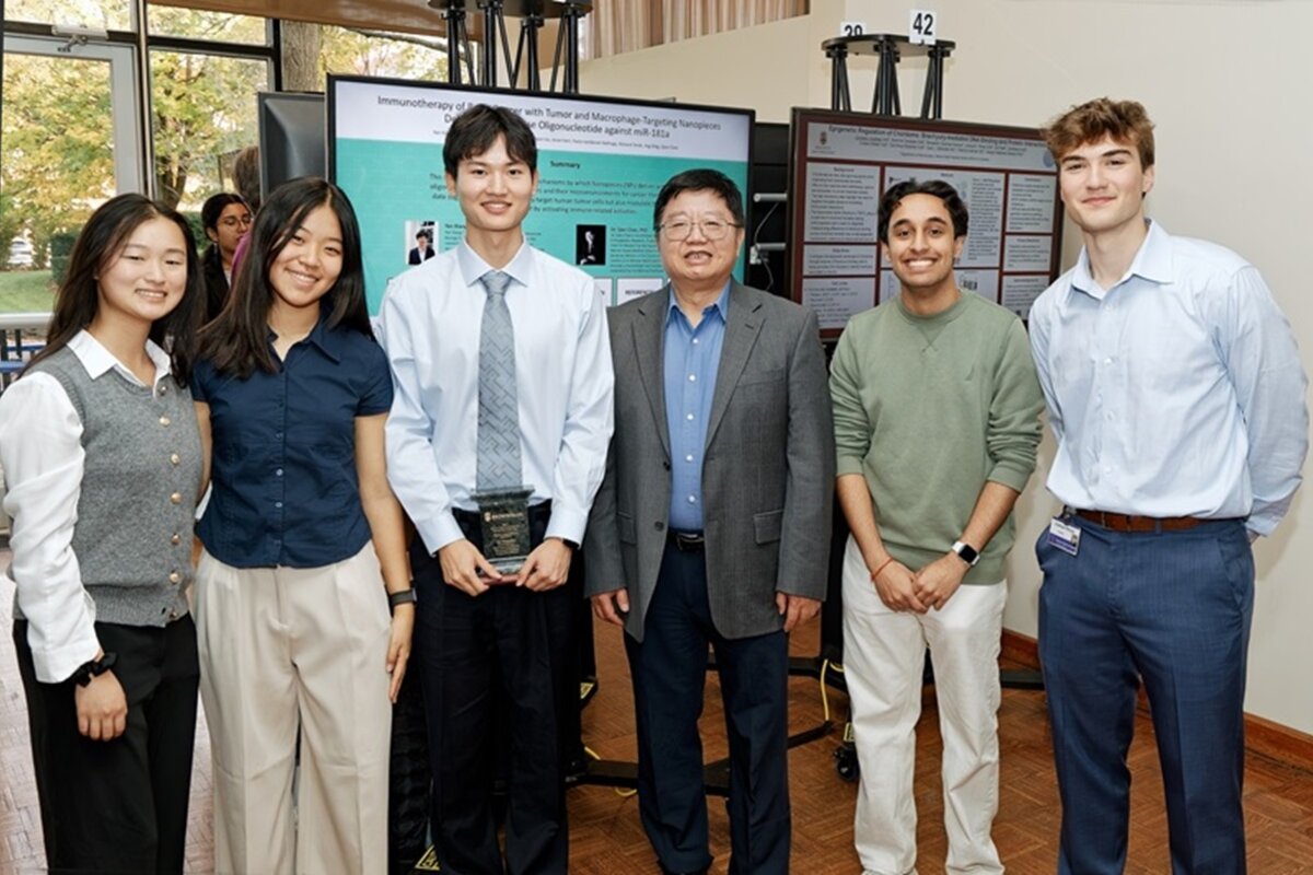 Six attendees pose for camera in front of digital poster