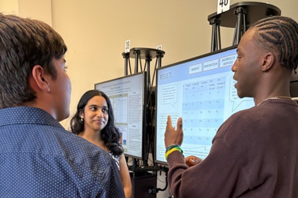 Three attendees discuss a digital poster and gesticulate