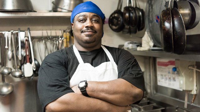 Man in restaurant kitchen wearing apron and smiling with arms crossed