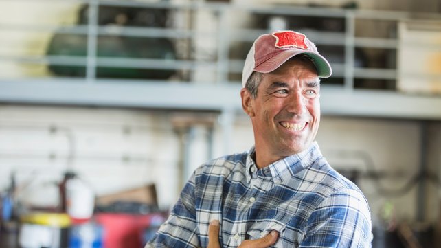Man in warehouse wearing hat smiling with arms crossed