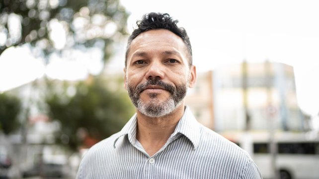 Man in striped shirt looking at camera outdoors with building in background