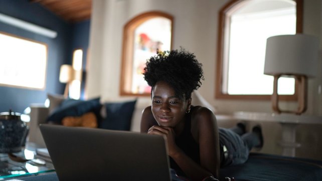 Teen in bedroom laying on bed and looking at laptop
