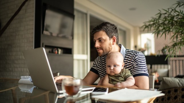Man  with baby on lap at kitchen table looking at laptop