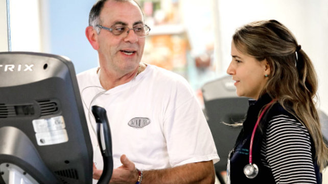 Man on exercise machine talking with medical employee