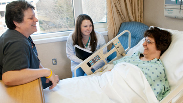Two hospital staff members chat with a patient in her hospital room