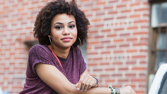 A teenage girl stands outside a brick building.
