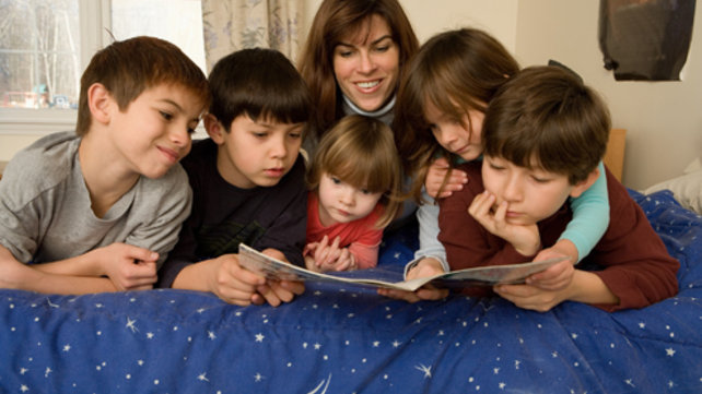 Smiling group of children reading a book with an adult