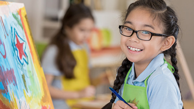 A young girl smiles as she stands in front of a painting she is creating.
