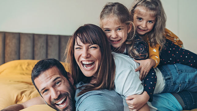 Two adults and two young children laughing as they sprawl across a bed.