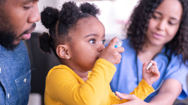 A child uses an inhaler as her parents watch.