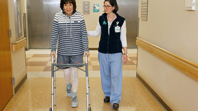 A patient walks with a physical therapist after surgery.