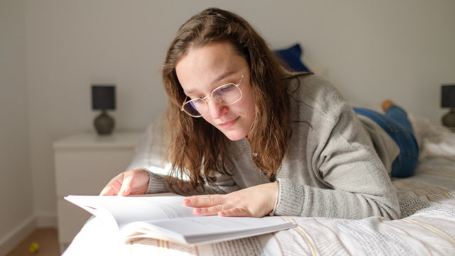 Adult laying on a bed and looking at a book