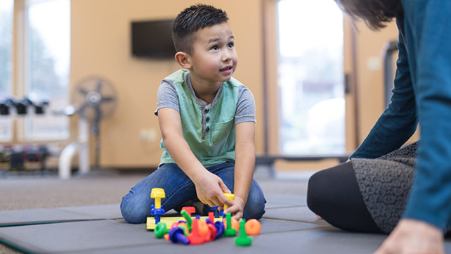 A child plays with toys with an adult watching.