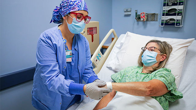 A female perioperative nurse standing at the bedside of  a female patient
