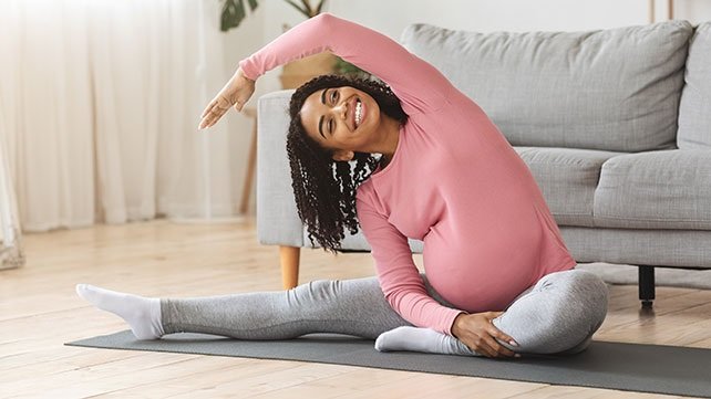 Pregnant woman sittign on her living room floor and stretching
