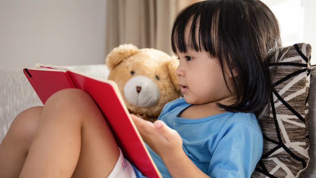 A young child reads to a teddy bear.