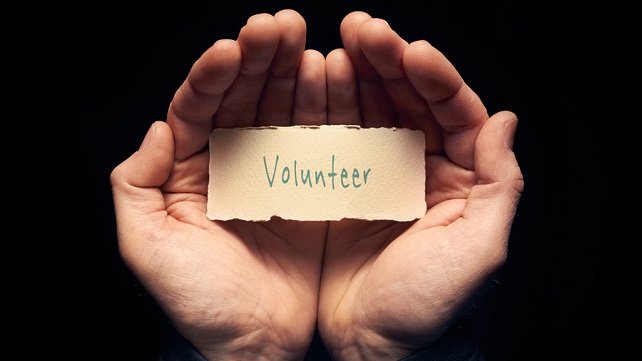 Two hands cupped together, holding a card that says "Volunteer"