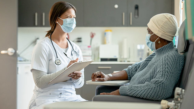 A clincian takes notes while talking with a hospital patient.