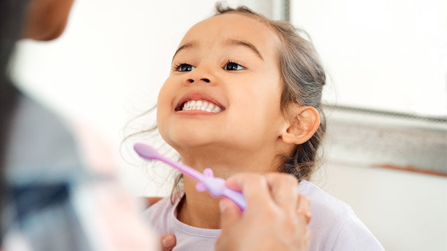 Child smiling up at adult holding a toothbrush