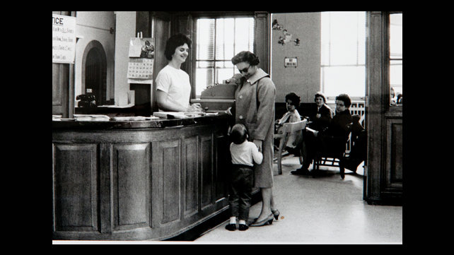 Historical photo of opening of Samuels Sinclair Dental Center of a woman checking her son in at the receptionist