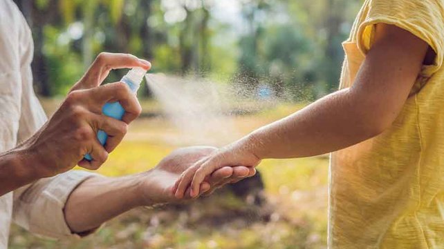 Mother spraying bug repellant on child