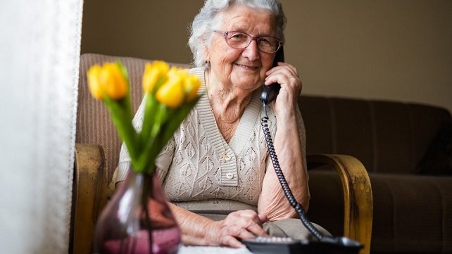 Elderly woman sitting on her couch and happily talking on her phone