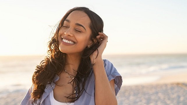 Smiling woman at the beach, holding back her hair from her face in the wind