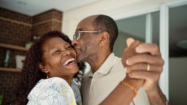An older woman and man smiling and dancing in their house