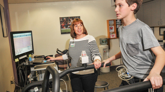 A boy walks on a treadmill as a medical clinician looks on.