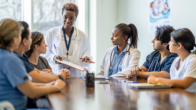 Female medical practitioner speaking at the head of a table of professionals