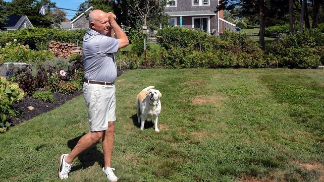 Tom Cioffi practicing his golf swing, accompanied by one of his dogs.