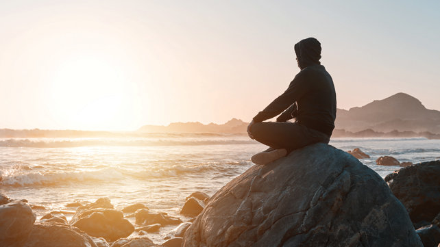 Person sitting on a rock, meditatively looking out to the ocean.