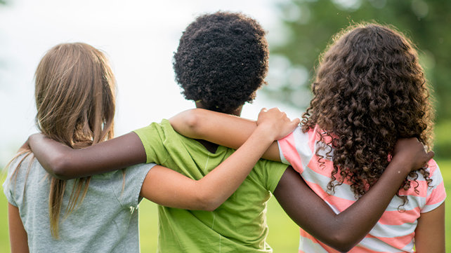 Three children with their arms over one another's shoulders, facing away from the camera.