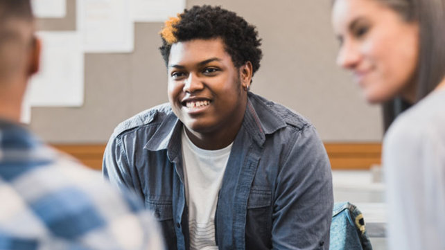 a group of teens sit in a circle talking.