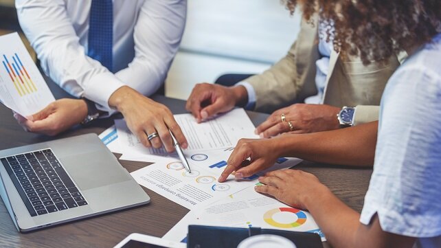 Professionals sitting around a desk in an office setting reviewing tables and graphs.