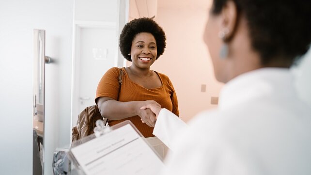 A smiling female patient shaking the hand of a medical professional.