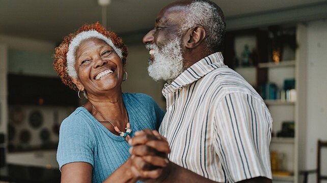 A smiling older couple dancing in their house.