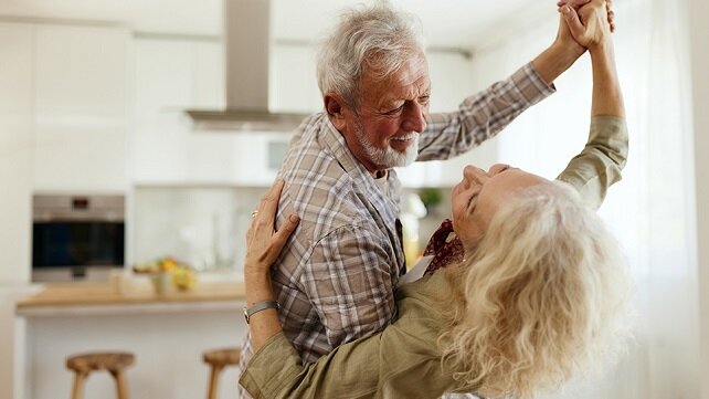 A smiling older couple dancing in their house.