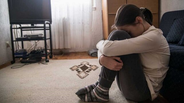 Stressed looking child sitting on their floor with their head in their knees.