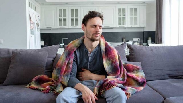 Man sitting on a couch clutching his stomch in pain