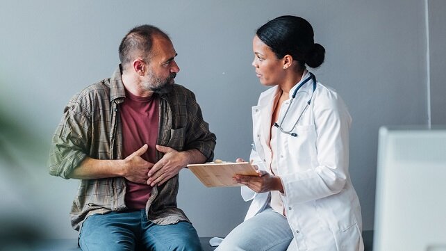 Patient with pained expression and holding his stomach sitting and talking to a doctor