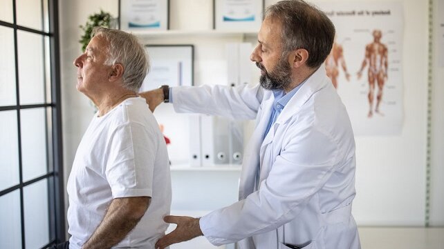 Doctor assisting an elderly patient who has ainful back problems.